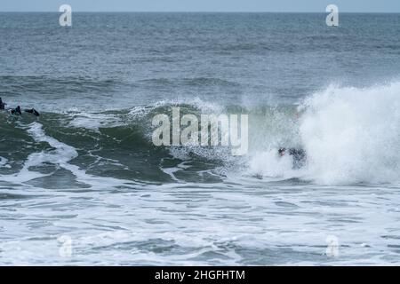 Bodyboarder effectuant un tour de tube surf océan ondulant vague de l'océan sur une journée d'hiver nuageux. Banque D'Images