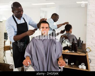 Le coiffeur africain coupe la cliente masculine Banque D'Images