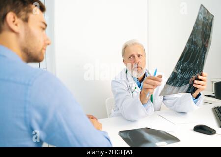 Vue de l'arrière du médecin radiologue adulte expliquant les résultats de l'examen IRM pour les patients jeunes hommes, montrant un cliché avec des images, Banque D'Images