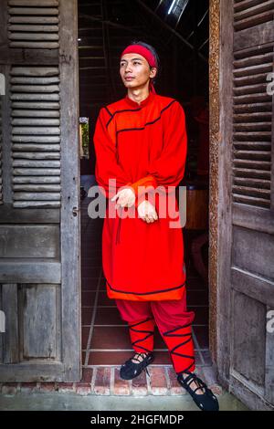 Un jeune homme vietnamien se tient dans la porte portant sa tenue rouge pour Hoi an impression. Banque D'Images