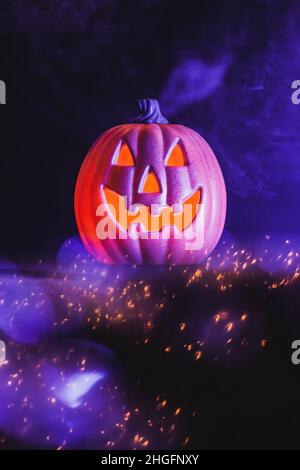 Une citrouille-lanterne souriante, aux reflets scintillants et au brouillard violet fantomatique, attend les amateurs de jeux d'enfant le soir d'Halloween. Banque D'Images