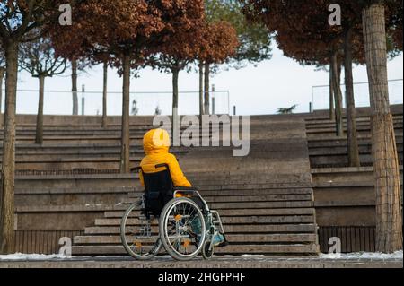 Femme en fauteuil roulant devant les escaliers dans la rue en hiver. Banque D'Images