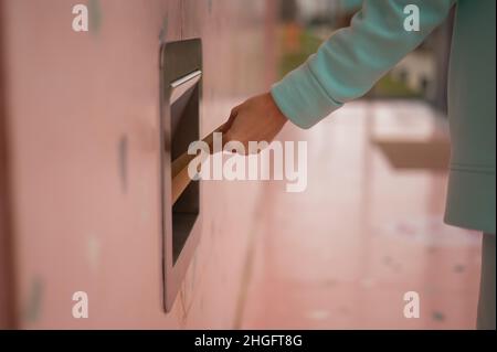 Une femme jette un sac de papier kraft dans un trou d'ordures dans un mur de café. Banque D'Images