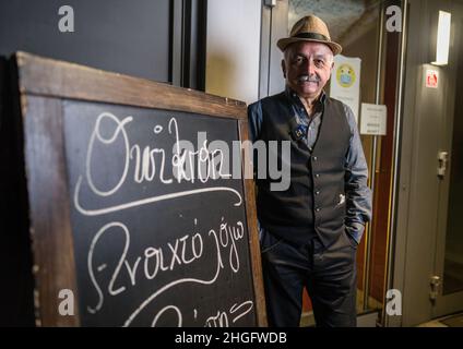 PRODUCTION - 14 janvier 2022, Hessen, Francfort-sur-le-main: Kostas (Konstantinos) Tsapakidis se tient dans la soirée à l'entrée de son restaurant grec appelé 'Taverna Omikron' dans le quartier de Bockenheim, qu'il court depuis environ 30 ans.a gauche, un panneau en grec accueillant les visiteurs.(À dpa 'Taverna 'Omikron', Ice café 'Corona' - les noms des entreprises et la pandémie') photo: Frank Rumpenhorst/dpa/Frank Rumpenhorst/dpa Banque D'Images