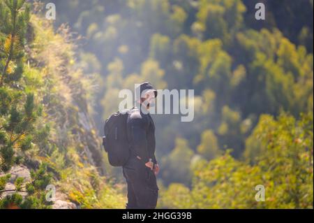 jeune homme robuste barbu en vêtements noirs avec sac à dos lors de la randonnée dans la forêt de montagne Banque D'Images