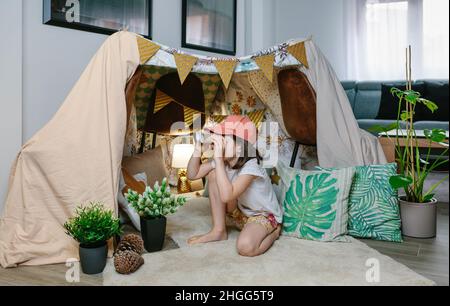 Petite fille jouant avec des jumelles en carton tout en campant à la maison dans le salon Banque D'Images