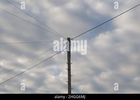 La moitié supérieure d'un poteau téléphonique avec des fils rayonnant dans différentes directions silhoueté contre un ciel nuageux Banque D'Images