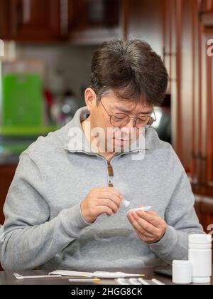 Homme asiatique d'âge moyen effectuant un test d'antigène rapide pour le COVID-19 à la maison. Banque D'Images