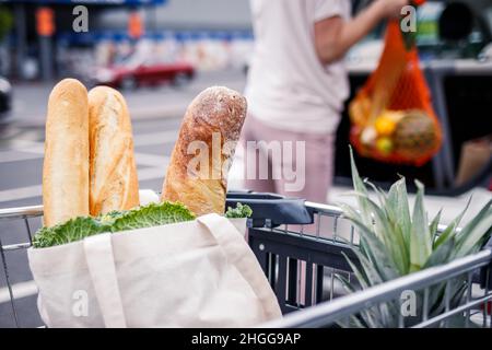 Pain et baguettes dans le panier.Femme chargeant des articles d'épicerie dans des sacs en filet réutilisables dans le coffre de voiture.Zéro déchet et shopping sans plastique Banque D'Images