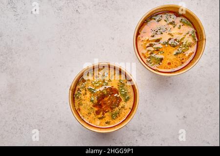 Soupe Tom Yam au saumon et aux fruits de mer dans deux récipients solides en papier sur fond clair.Concept de restauration design à emporter ou à livrer Banque D'Images
