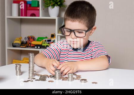 Un enfant en lunettes, un jeune homme d'affaires joue avec des pièces de monnaie et économise de l'argent. Banque D'Images