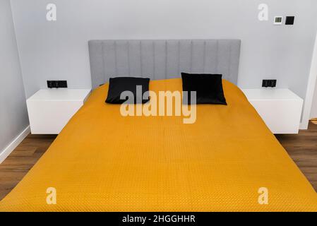 Un lit dans une chambre moderne avec un couvre-lit à la moutarde, look simple. Banque D'Images