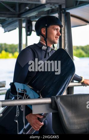 Un wakeboarder plein de sourires et plein d'équipement avec une planche sur le quai de départ Banque D'Images