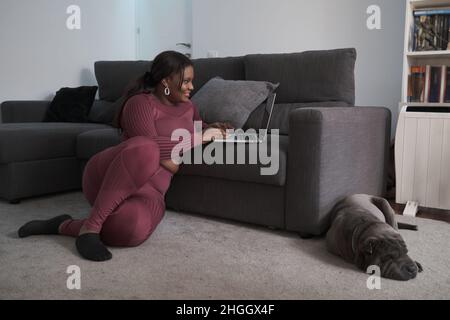 Femme africaine de vêtements de sport assise sur le sol à l'aide d'un ordinateur portable à la maison. Banque D'Images