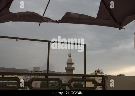 Vue sur une mosquée d'Aqaba, en Jordanie, avec un ciel bleu grisâtre à la mer Rouge à travers un parapluie déchiré qui s'envole au lever du soleil. Banque D'Images