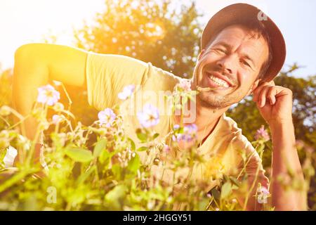 Heureux homme en chapeau assis sur la prairie parmi les fleurs colorées dans la nature en été Banque D'Images