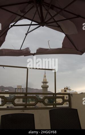 Vue sur une mosquée d'Aqaba, en Jordanie, avec un ciel bleu grisâtre à la mer Rouge à travers un parapluie déchiré qui s'envole au lever du soleil. Banque D'Images