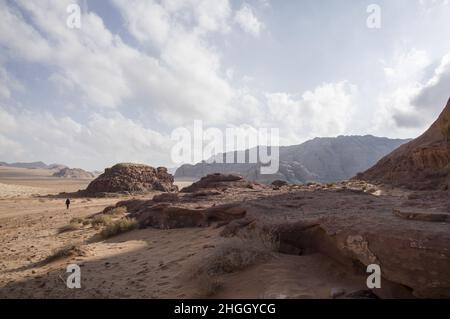 Attraction touristique Wadi Rum en Jordanie avec une seule personne de derrière dans le vaste paysage désertique avec des canyons et des sables rouges et des cieux bleus nuageux Banque D'Images