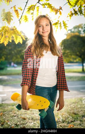 Portrait vertical de style de vie en plein air d'une jeune fille adolescente souriante avec un skateboard jaune portant une chemise à carreaux rouge Banque D'Images