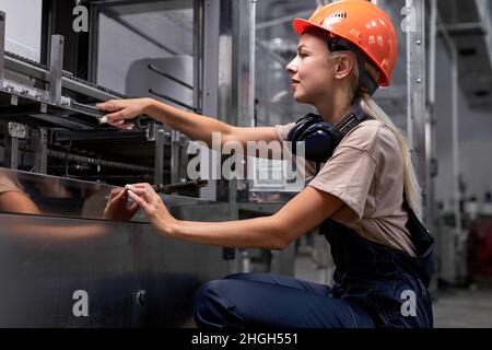 Une femme qualifiée répare des équipements cassés en usine à l'aide d'une clé, une femme en uniforme et un casque est concentrée sur le travail, en regardant confiant et profess Banque D'Images