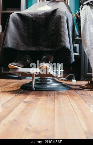 Un client en gros plan du salon de coiffure est assis sur une chaise tout en étant servi par un coiffeur Banque D'Images