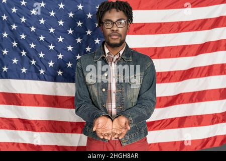 Les Afro-Américains pauvres demandent de l'argent à l'État.Guy se tient avec les mains pliées mendiant dans le drapeau américain arrière-plan .vie sur les prestations de chômage.Pauvre immigrant.Gros plan .espace de copie.Photo de haute qualité Banque D'Images