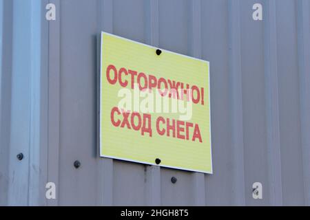 L'inscription sur la plaque : attention, chute de neige. Avec précaution, la neige tombe des toits, le panneau d'avertissement sur le mur. Étiquette d'avertissement en russe. Grandes lettres rouges sur une plaque jaune sur fond gris. Banque D'Images