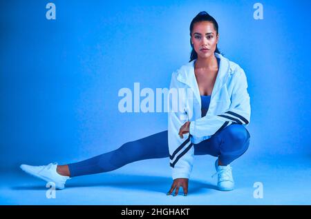 Je n'oublie jamais de m'étirer.Portrait complet d'une jeune athlète féminine attirante qui s'étire avant un entraînement sur fond bleu. Banque D'Images