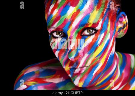 Vivez la vie de manière vivante.Photo studio d'une jeune femme posant avec une peinture de couleur vive sur son visage sur un fond noir. Banque D'Images