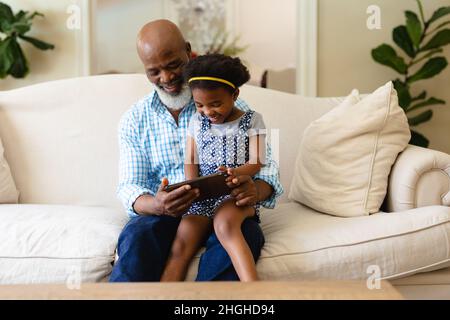 Grand-père et petite-fille afro-américains utilisant une tablette numérique assis sur un canapé à la maison Banque D'Images