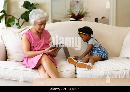 Grand-mère afro-américaine utilisant une tablette numérique et sa petite-fille utilisant un ordinateur portable sur un canapé Banque D'Images