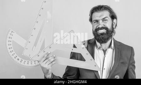 homme barbu mature enseignant en costume assis dans la classe d'école avec tableau noir, mesure Banque D'Images