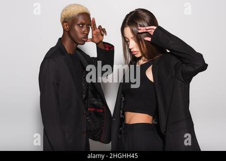 jeune et élégant couple interracial en noir posant sur le gris Banque D'Images