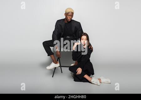 homme afro-américain blond regardant la caméra près d'une femme assise sur un gris avec ombre Banque D'Images