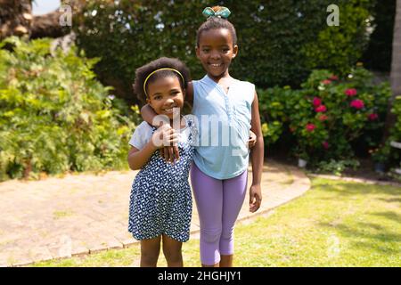 Portrait d'une jeune fille afro-américaine souriante debout avec le bras autour de la petite sœur à l'arrière-cour Banque D'Images