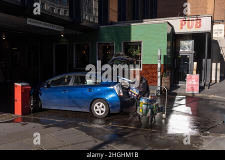 Un homme déleste les fournitures d'une voiture garée et sur un petit chariot, à l'arrière des boutiques de la City de Londres, le quartier financier de la capitale, le 20th janvier 2022, à Londres, en Angleterre. Banque D'Images