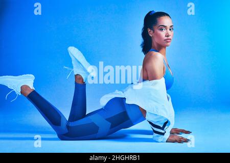 Coupe et féminité.Portrait en longueur d'une jeune athlète féminine attrayante posant sur le sol sur un fond bleu. Banque D'Images