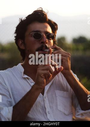 Jeune homme en lunettes de soleil jouant de la harpe à la bouche au coucher du soleil Banque D'Images