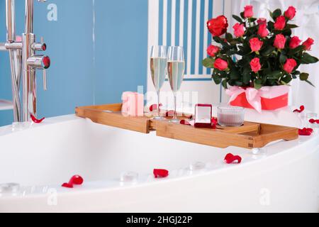 Plateau avec anneau de fiançailles, verres de champagne et bougies sur la baignoire dans la chambre décorée pour la Saint-Valentin Banque D'Images