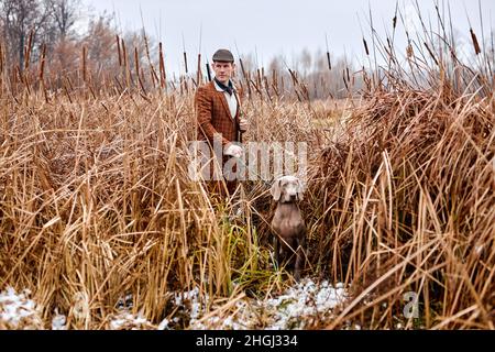 jeune américain de race blanche poacher ou chasseur en chapeau avec une arme à feu et weimaraner chien race ami dans la nature de campagne.Incroyable matin d'automne. Animaux et Banque D'Images