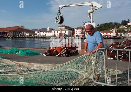 Pêcheur local réparant ses filets de pêche sur le quai du port de St Jean de Luz, pays Basque, Nouvelle Aquitaine Banque D'Images