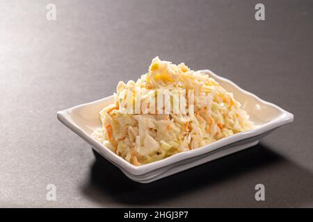 Salade fraîche crémeuse de coleslaw au chou et à la carotte servie dans un plateau blanc sur fond gris foncé vue du dessus Banque D'Images