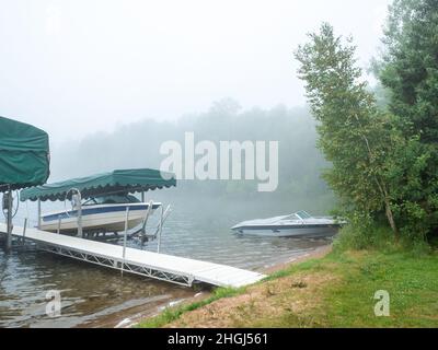 Belle scène de lac du Minnesota au cours d'une matinée brumeuse avec des eaux calmes et quelques bateaux de plaisance sur la rive. Banque D'Images