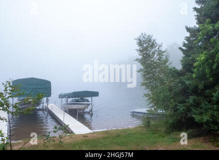 Une matinée brumeuse sur un magnifique lac du Minnesota, avec des eaux calmes, un quai et des bateaux de plaisance sur la rive et sur les remontées mécaniques. Banque D'Images