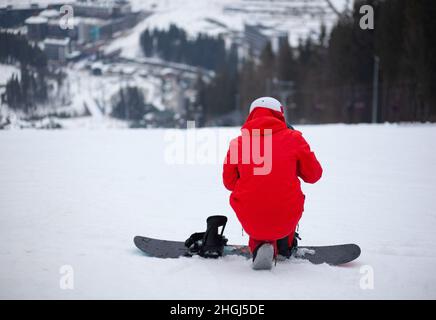 Un homme dans une veste rouge avec un snowboard se tient sur un flanc de montagne. Banque D'Images