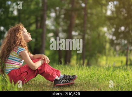 Une fille se reposant le matin dans le parc.Elle mit son visage au soleil, ferma les yeux et nourrit l'énergie de la nature, rêves, écoute le silence. Banque D'Images