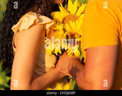 couple tenant un bouquet de tournesols debout ensemble dans un champ au soleil couchant, vacances d'été Banque D'Images