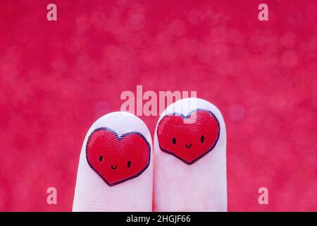 Des coeurs souriants du bout des doigts sur fond rouge.Concept d'amour créatif. Banque D'Images