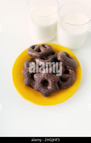 Les biscuits de pain d'épice enrobés de chocolat sont posés sur une assiette jaune avec un verre de lait.Place pour une inscription Banque D'Images