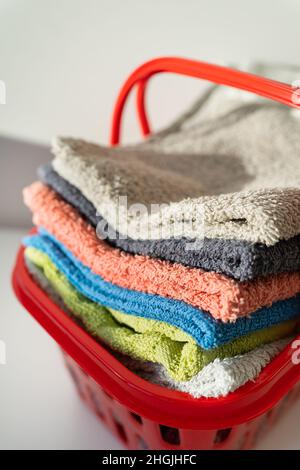 Les serviettes multicolores sont dans un panier à linge rouge sur fond blanc.Lavage et repassage des vêtements, vue du dessus Banque D'Images